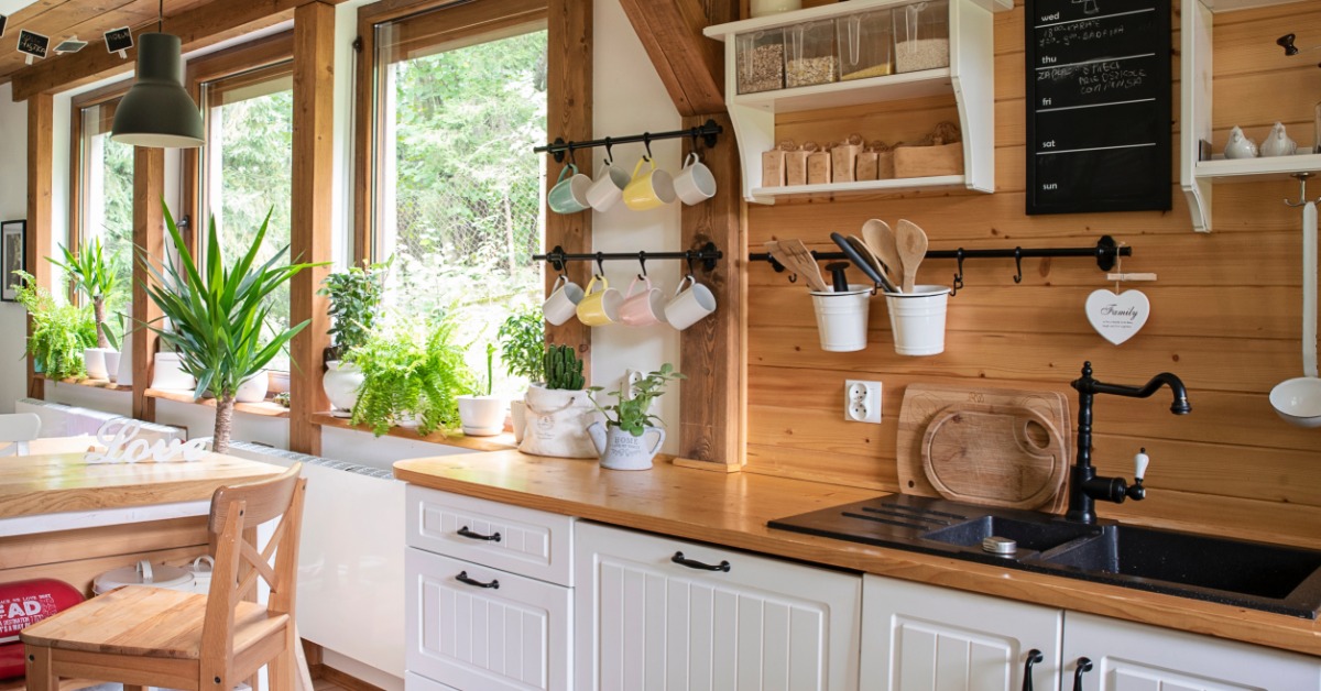 A rustic kitchen interior with white cabinets, wooden accents, vintage cookware, and a window letting in natural light.